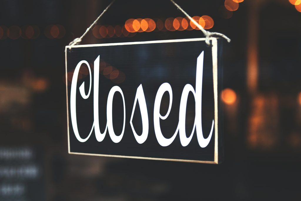 A close-up of a 'Closed' sign hanging against a blurred, bokeh background, creating a warm, inviting atmosphere.