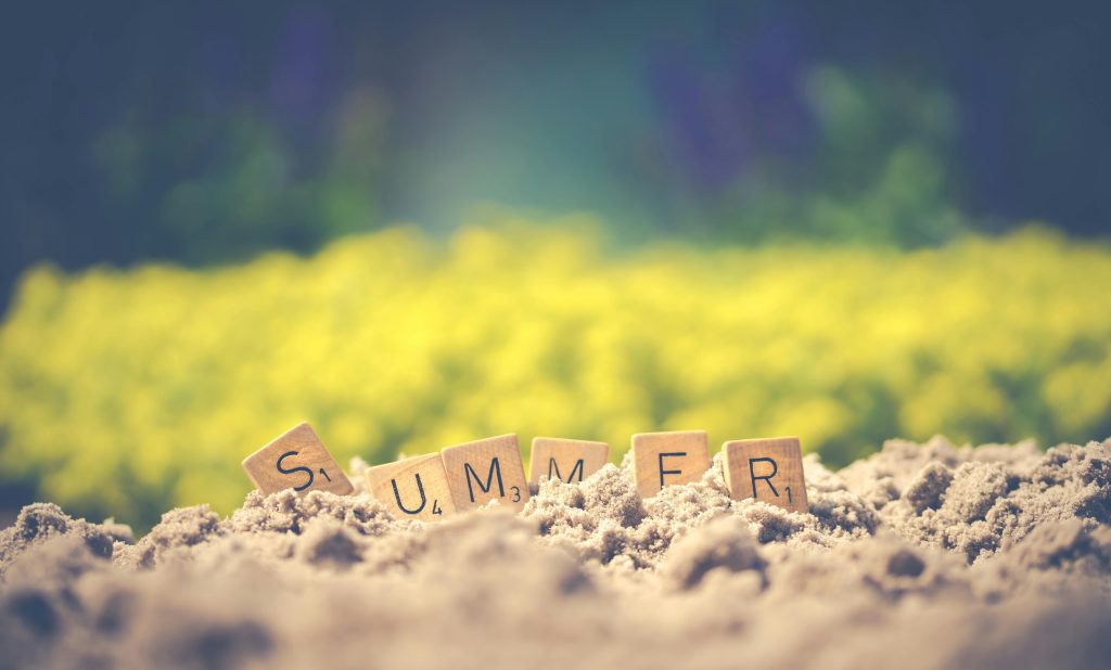 Scrabble tiles forming the word 'summer' in sand with a blurred background, evoking warm vibes.